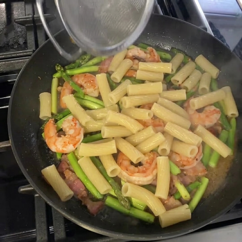 Rigatoni cocido siendo mezclado con los ingredientes en la sartén.
