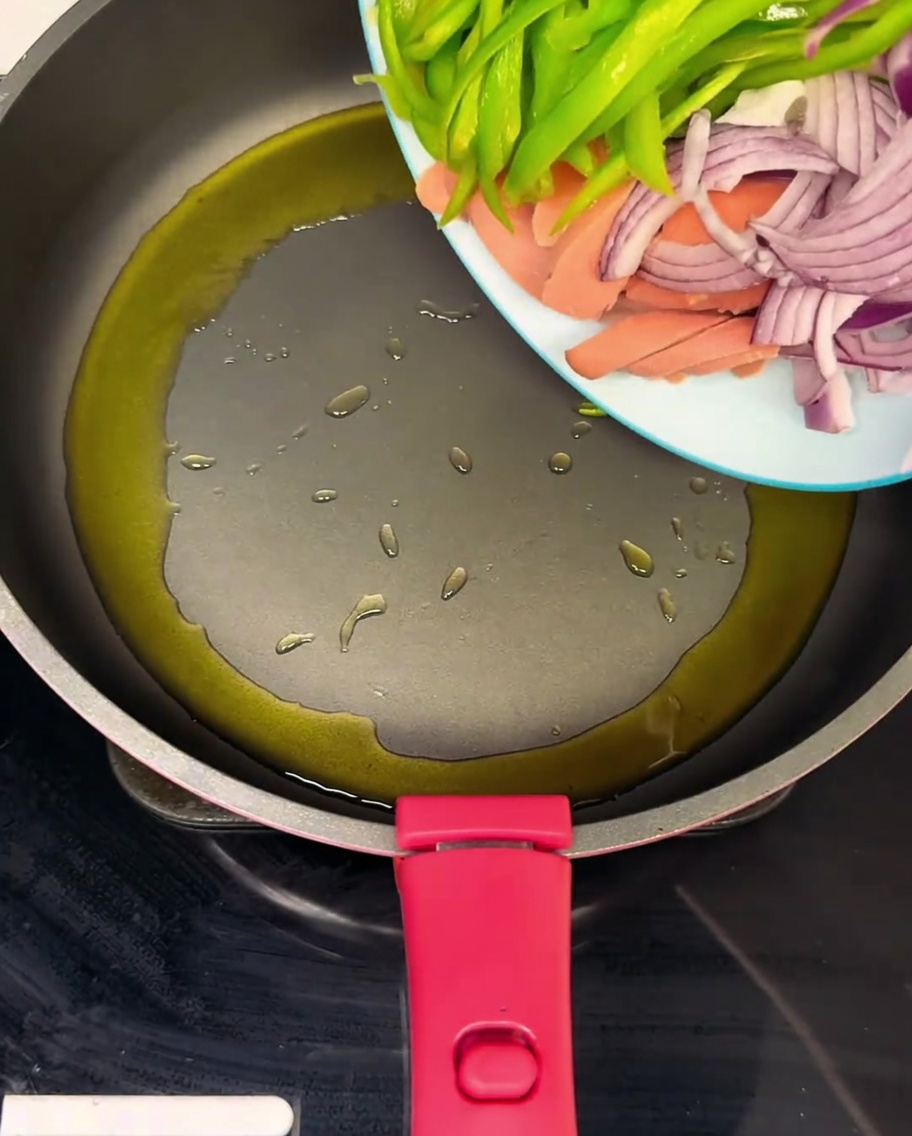 Una sartén caliente con jamón en rodajas, pimientos verdes y cebollas salteándose en aceite.