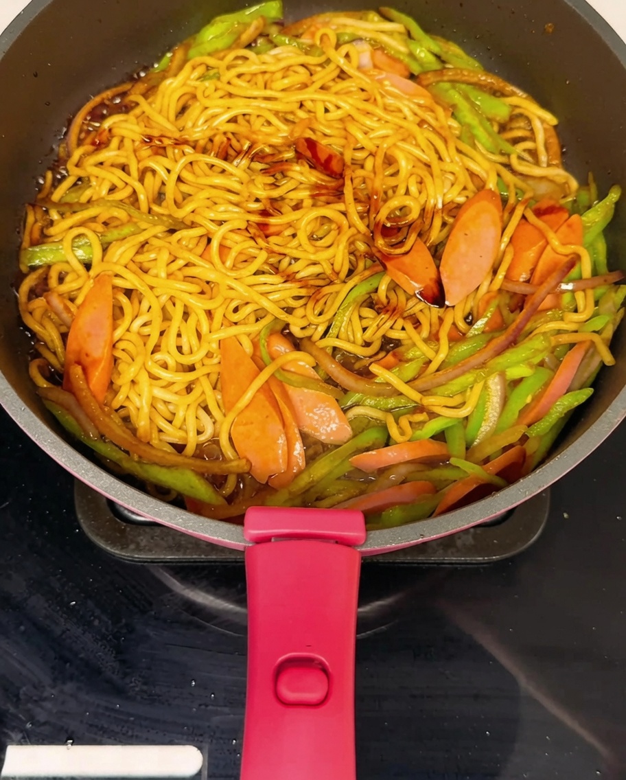 Fideos salteados en una sartén siendo sazonados con pimienta negra recién molida.