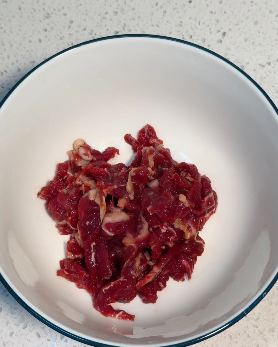 Tiras de ternera mezclándose con los ingredientes del marinado en un bol blanco.