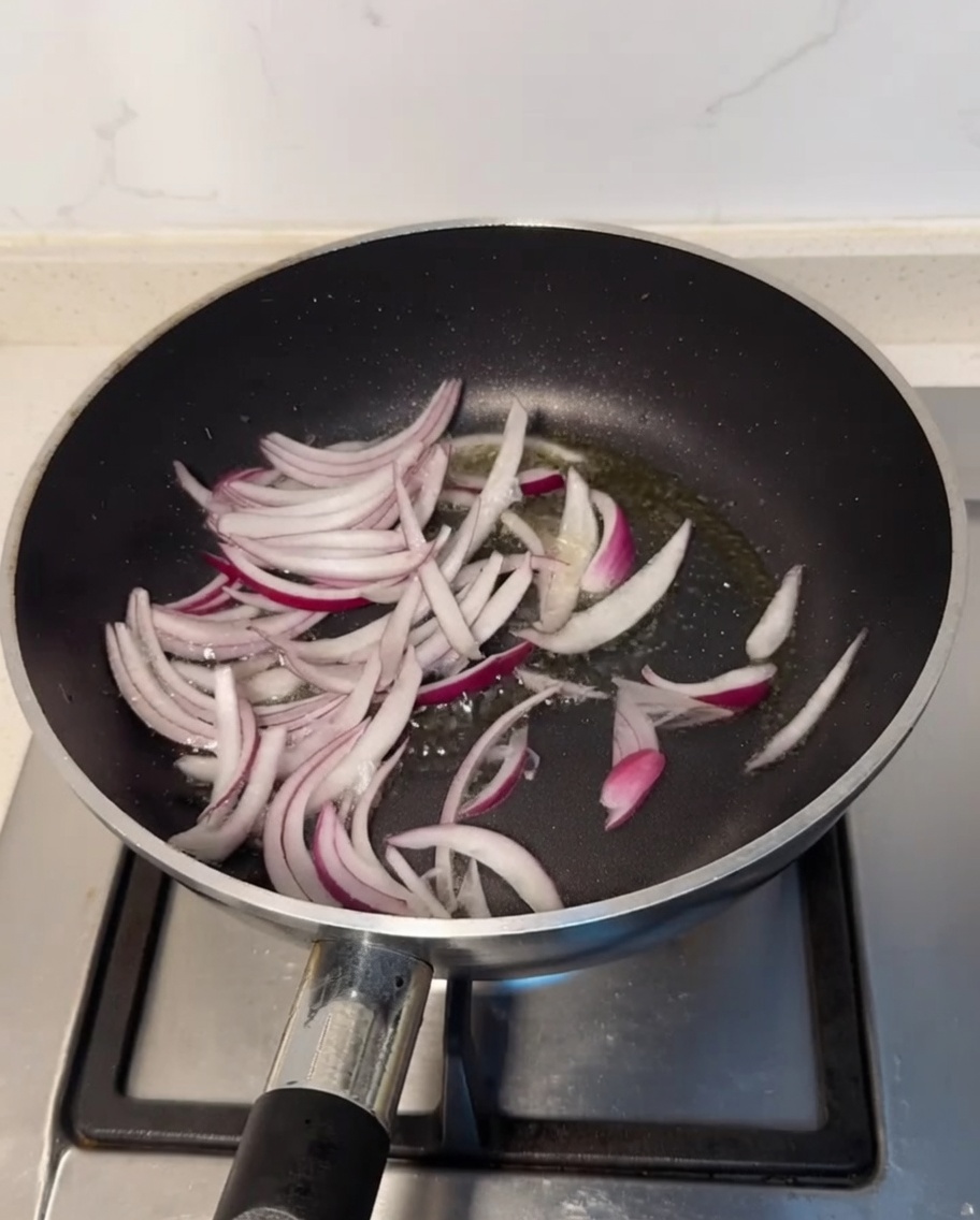 Trozos de cebolla morada chisporroteando en una sartén con aceite caliente.
