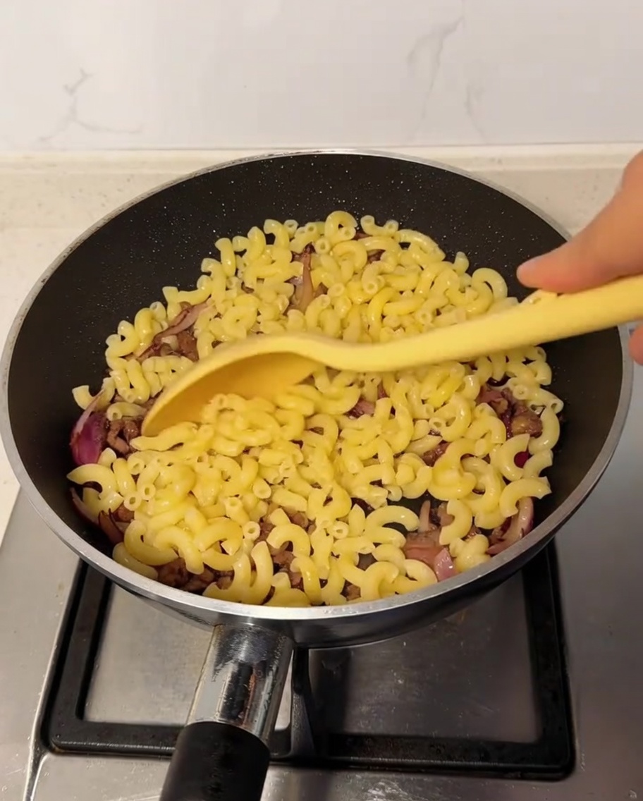 Macarrones cocidos incorporándose a la sartén con la mezcla de ternera y cebolla.