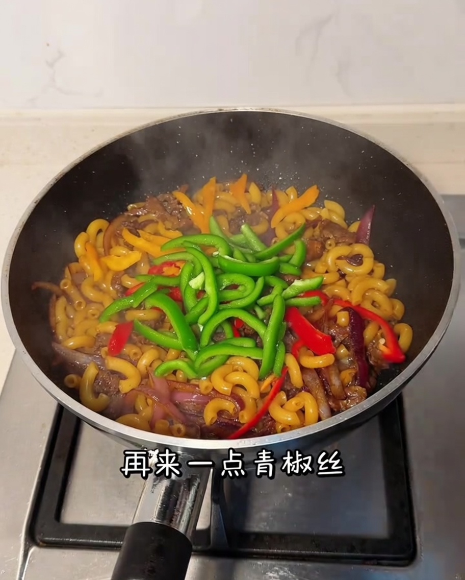 Pimiento verde en tiras siendo mezclado en la sartén con los macarrones y la ternera.