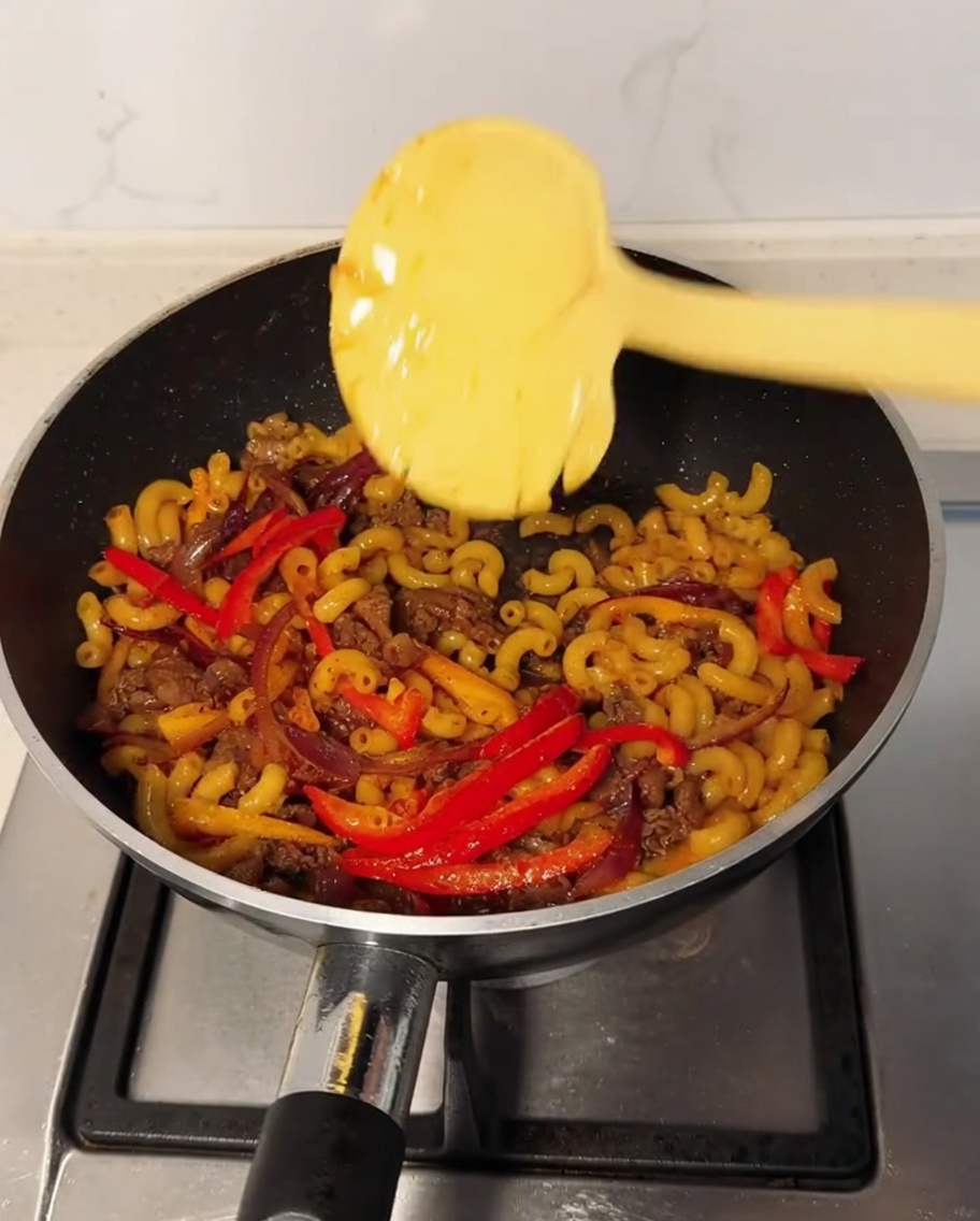 Una loncha de queso sobre la mezcla de macarrones en un wok con pimienta negra espolvoreada.