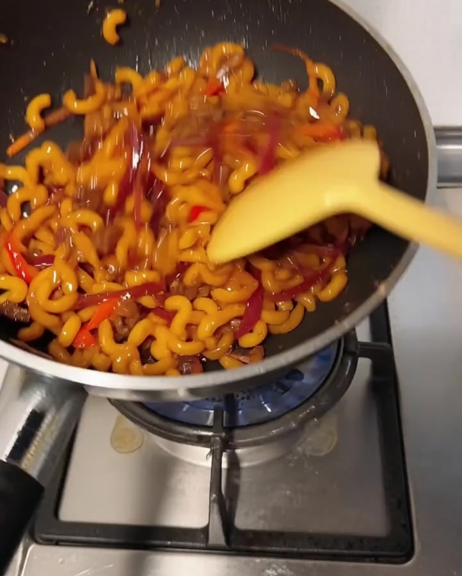 La mezcla de macarrones siendo removida en el wok mientras el queso se derrite.