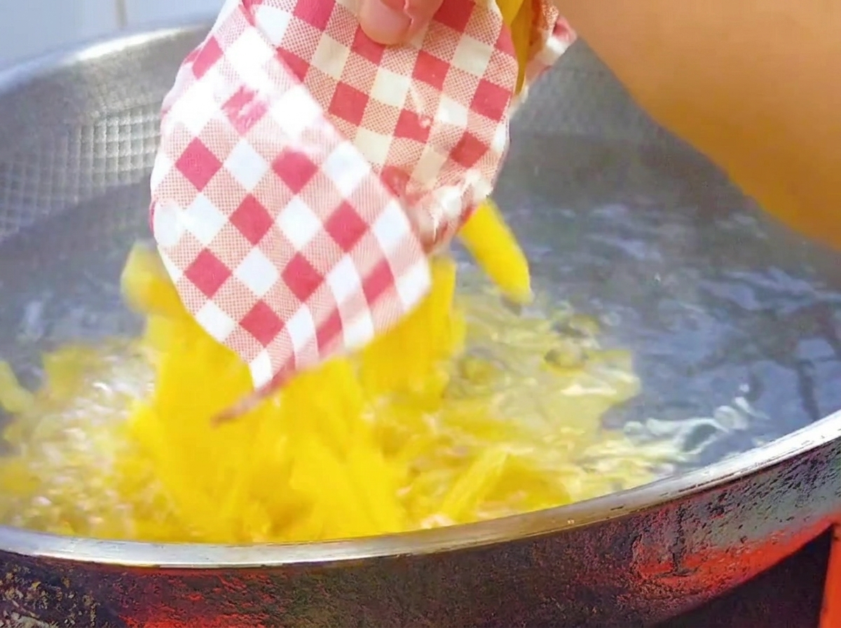 Pasta penne seca siendo vertida en un wok grande con agua hirviendo salada.