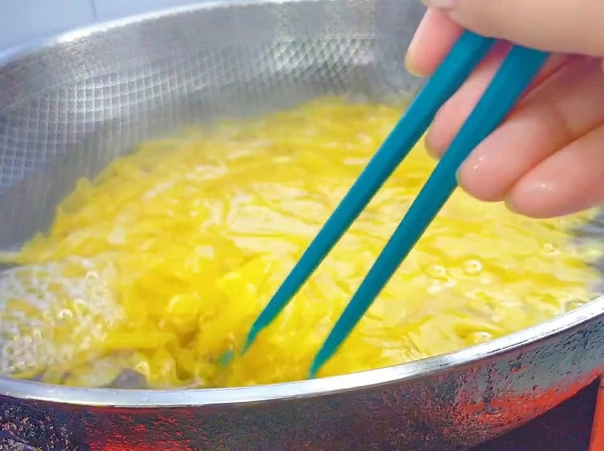 Palillos azules removiendo pasta penne hirviendo en un wok de acero inoxidable.