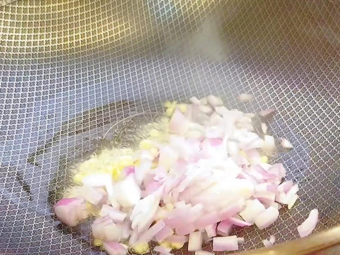 Ajo picado y cebolla troceada siendo salteados en un wok caliente con aceite.