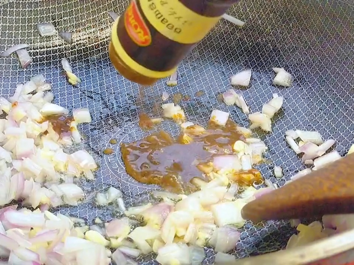 Salsa de pimienta negra siendo vertida desde una botella en un wok sobre aromáticos salteados.