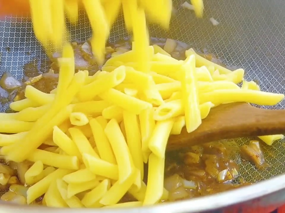 Pasta penne cocida siendo añadida al wok con la base de salsa de pimienta negra.