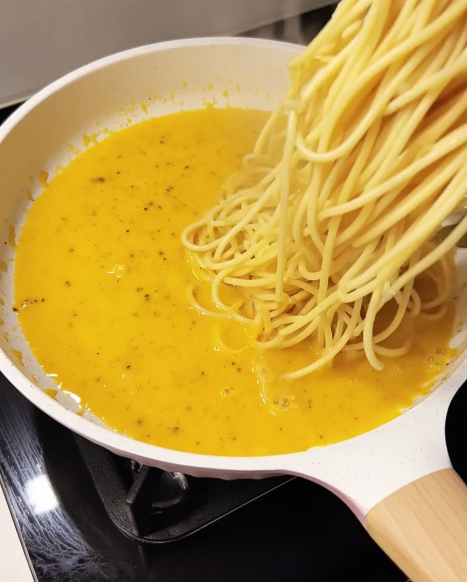 Espaguetis cocidos siendo añadidos a la salsa cremosa en la sartén.