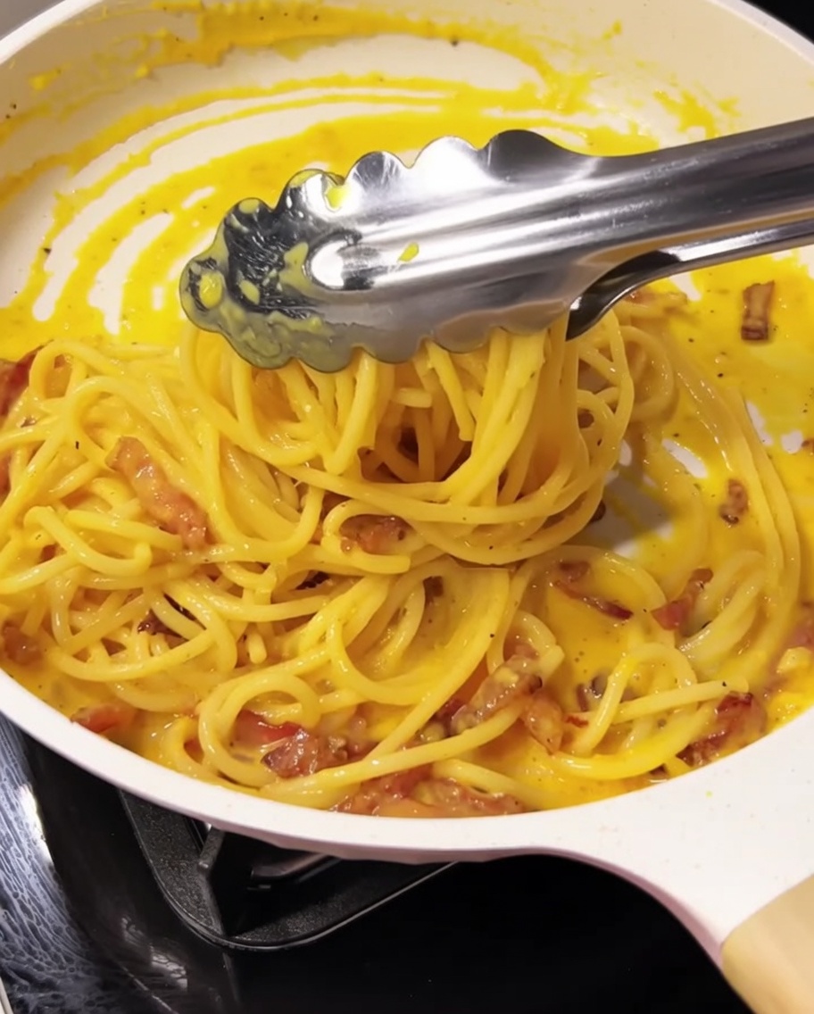 Pinzas mezclando los espaguetis con la salsa y el guanciale.
