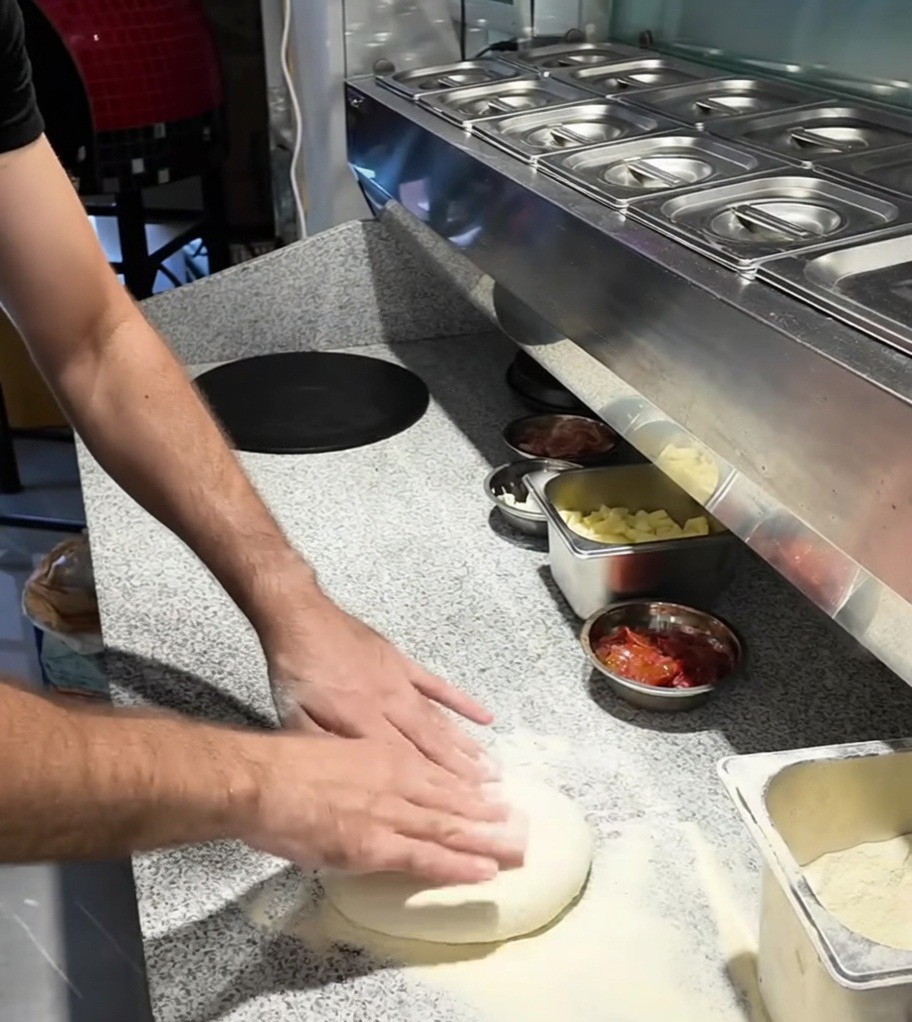 Manos estirando una bola de masa de pizza sobre una encimera enharinada.
