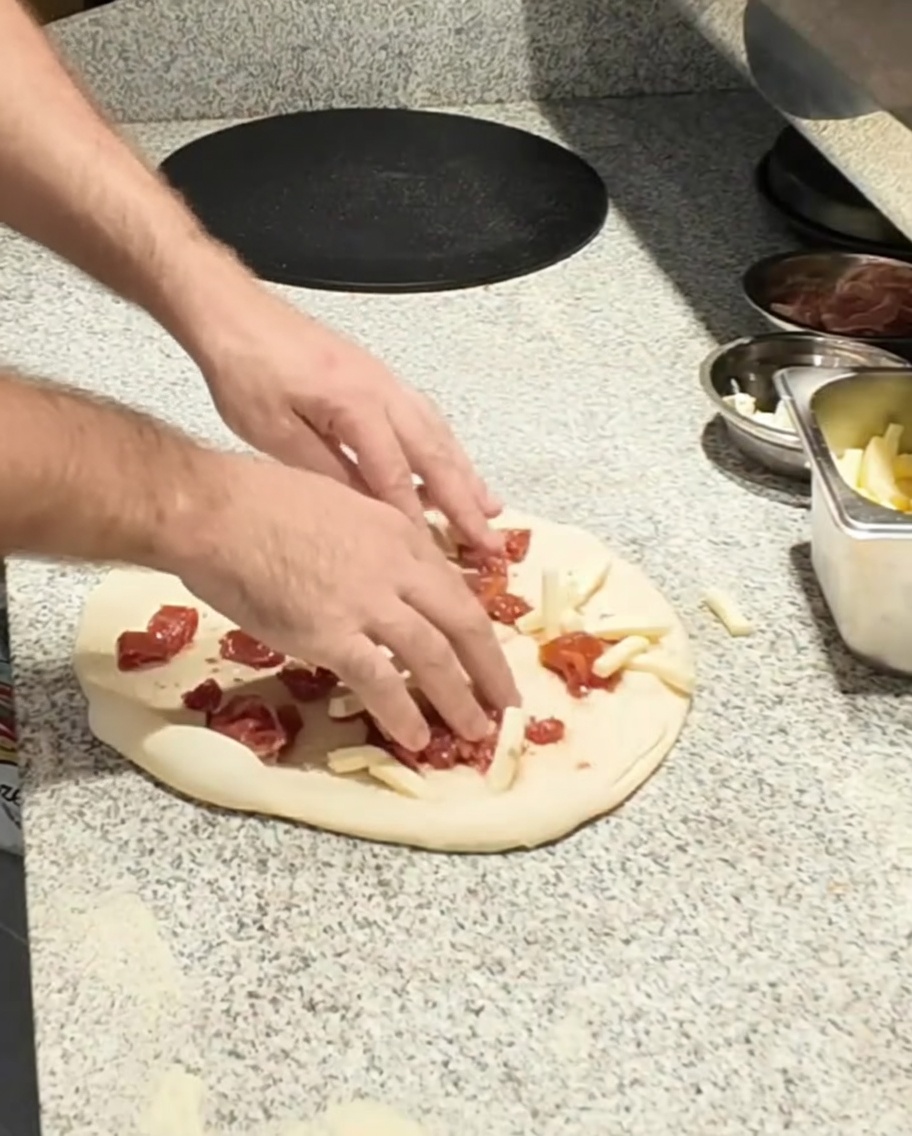 Queso mozzarella siendo añadido a la base de la pizza.