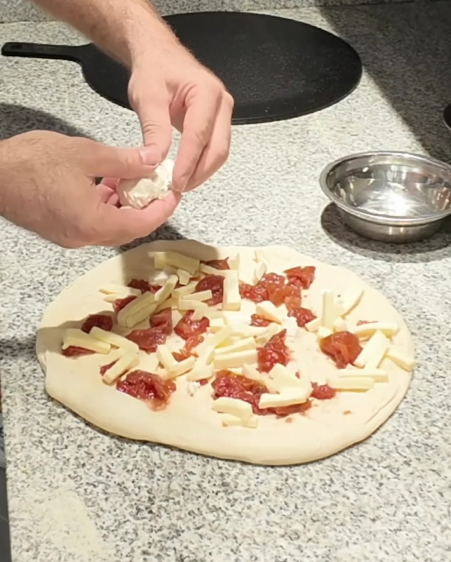 Queso de cabra fresco siendo colocado sobre la pizza.