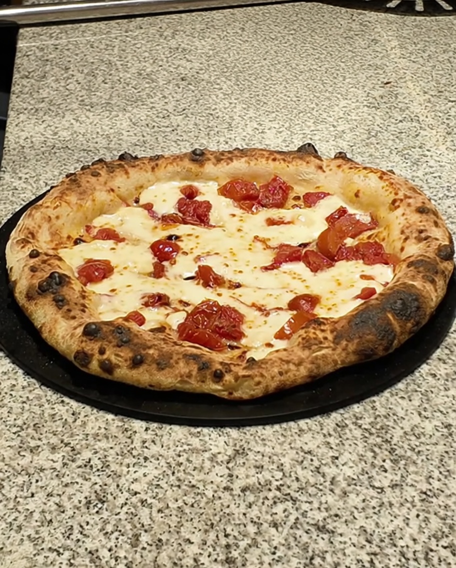 Pizza terminada sobre una superficie oscura siendo cubierta con lonchas de panceta.