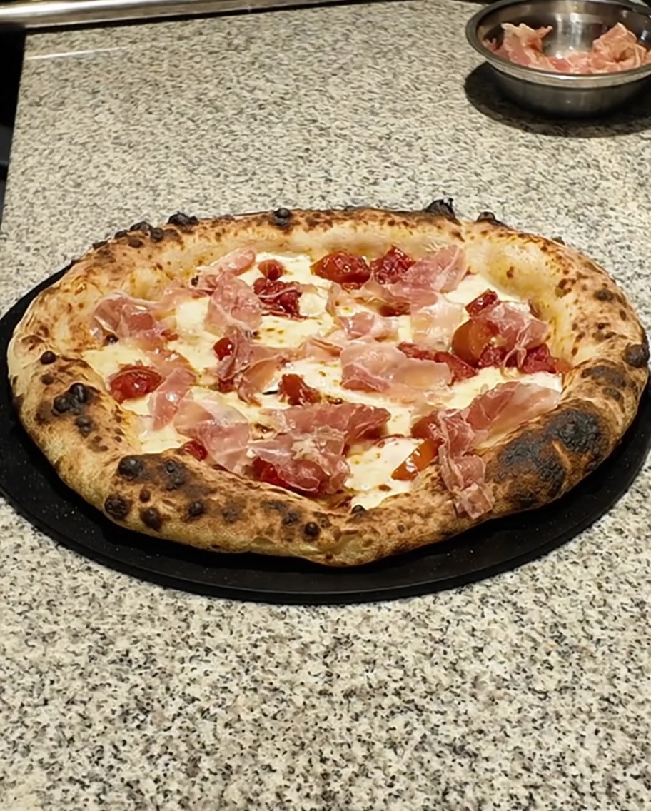 Primer plano de hojas de tomillo verde fresco siendo espolvoreadas sobre una pizza horneada.