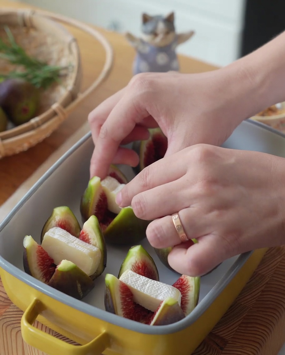 Higos en una fuente para hornear amarilla siendo rellenos con trozos de queso Brie.