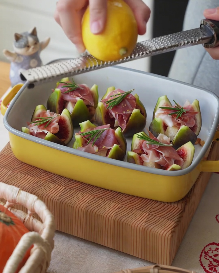 Limón fresco siendo rallado sobre una bandeja de higos rellenos de jamón.
