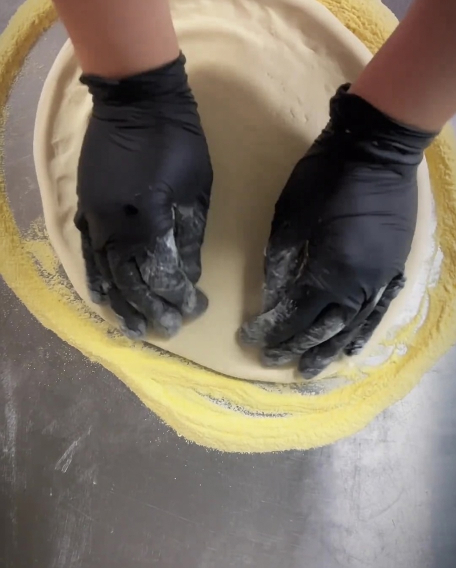 Un rodillo perforador pasándose sobre la base de la pizza para crear pequeños agujeros uniformes.