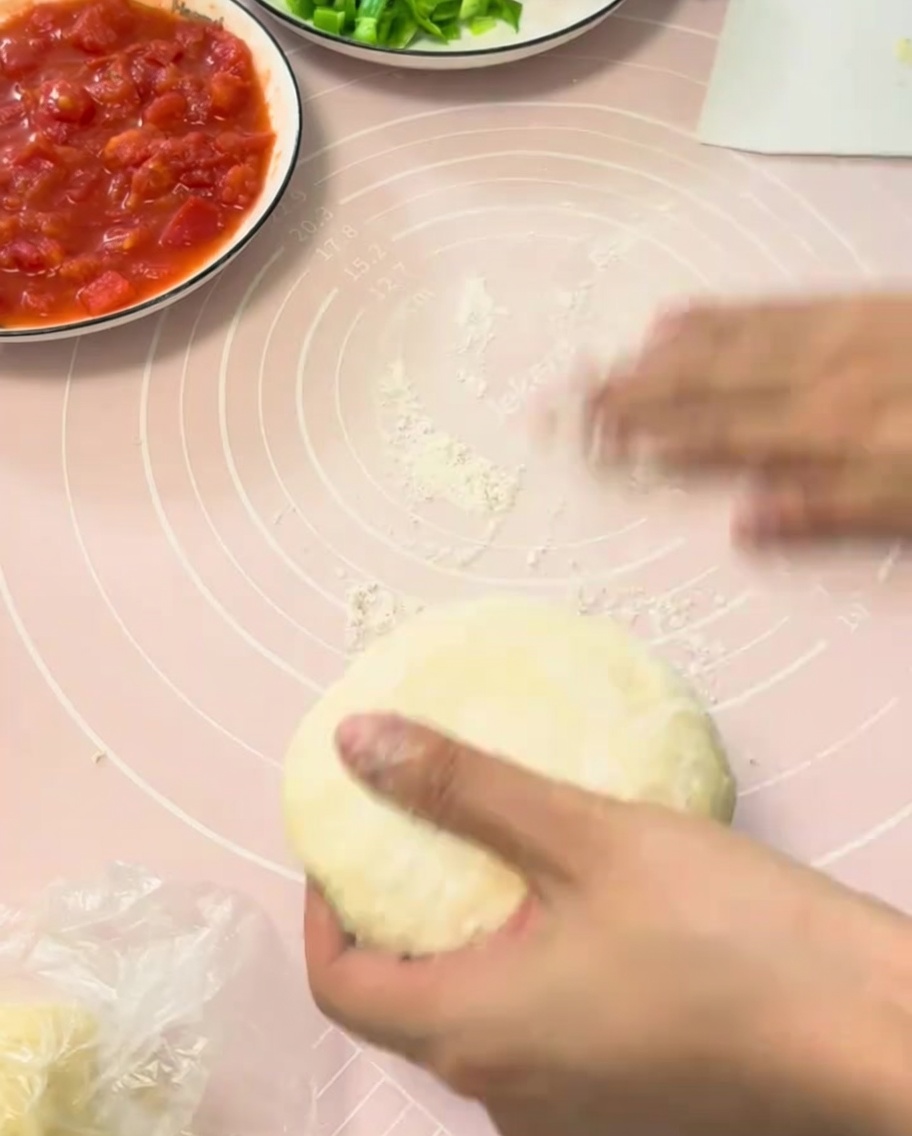 Un trozo de masa de pizza fermentada siendo estirada sobre un tapete de silicona rosa.