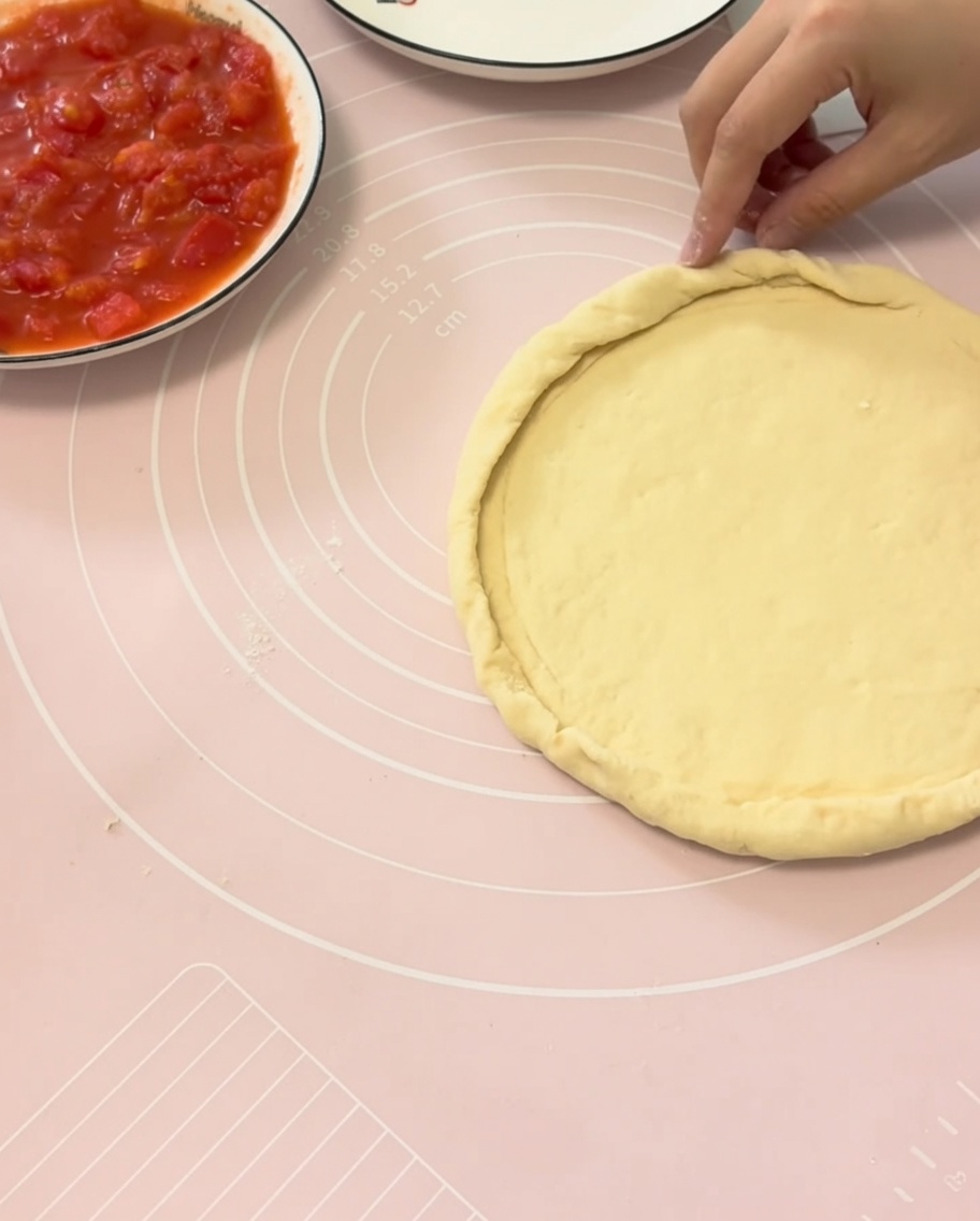 Manos doblando los bordes de la masa de pizza sobre un plato para formar una corteza perfecta.