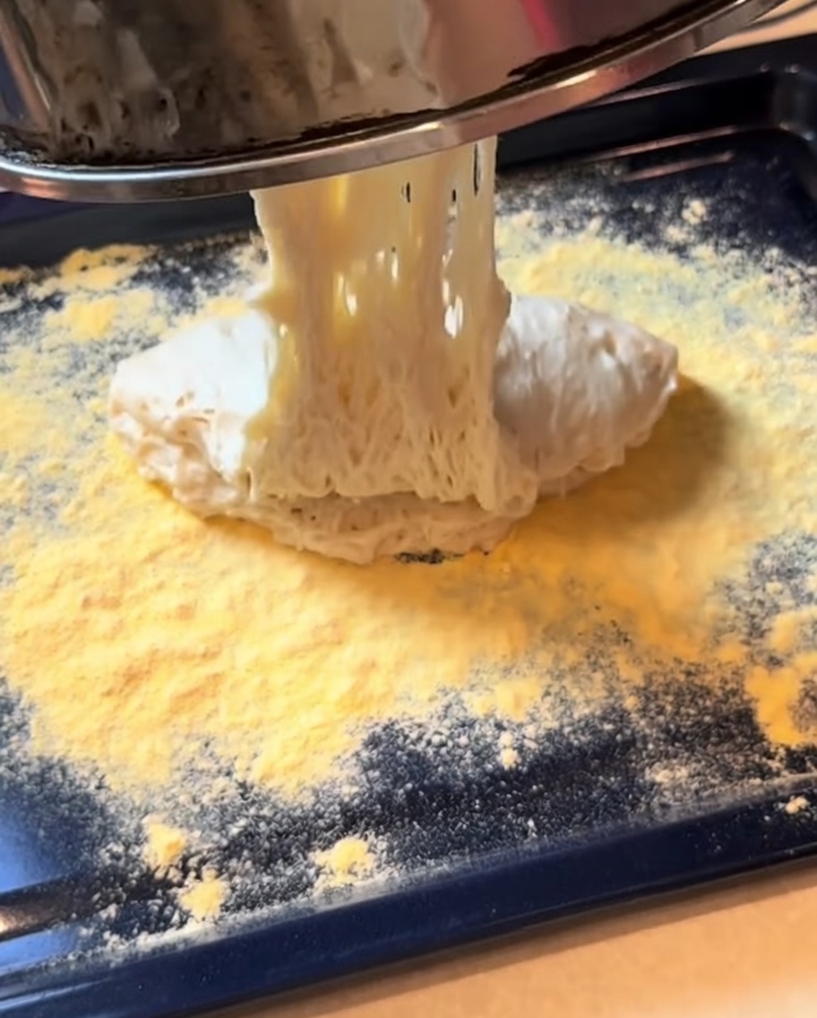 Masa de pizza fermentada siendo extendida en forma rectangular sobre una bandeja.