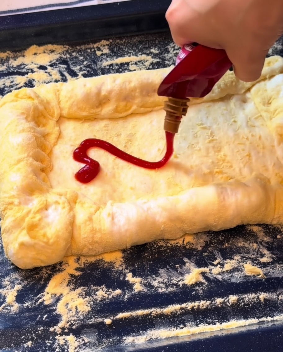 Ketchup extendido sobre la masa y cubierto con queso mozzarella rallado.