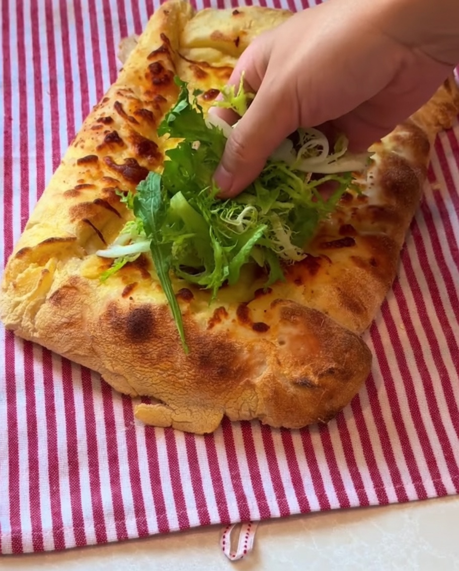 Hojas verdes y prosciutto colocados sobre la pizza recién horneada.