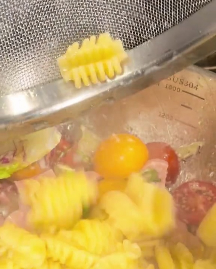 Pasta en espiral cocida transfiriéndose a un bol con verduras y jamón.