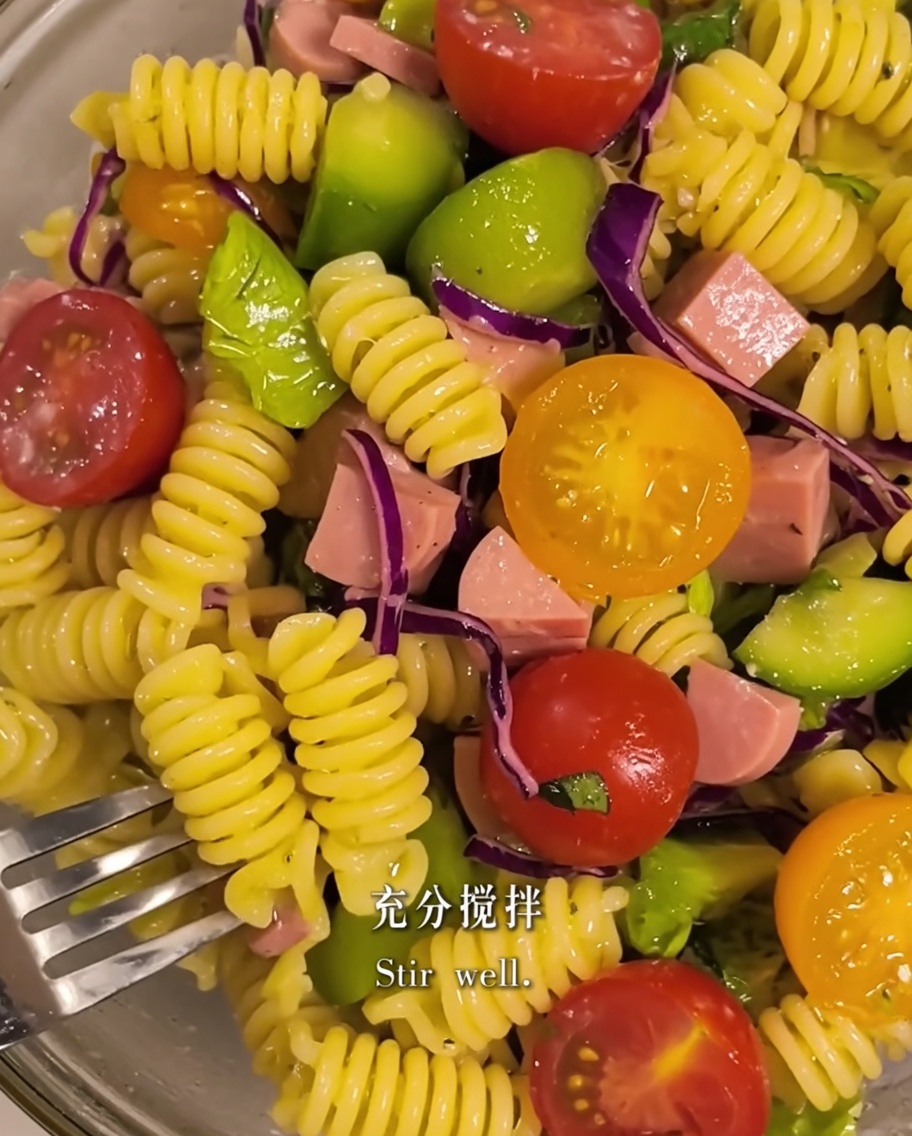 Ingredientes de la pasta y la ensalada siendo mezclados con aceite de oliva en un bol.