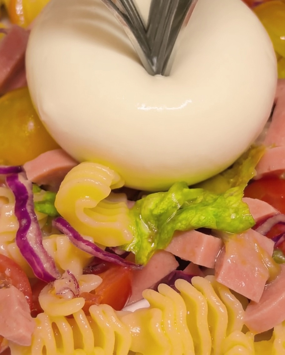 Una bola de queso burrata partiéndose con un tenedor para revelar su centro cremoso y fluido.