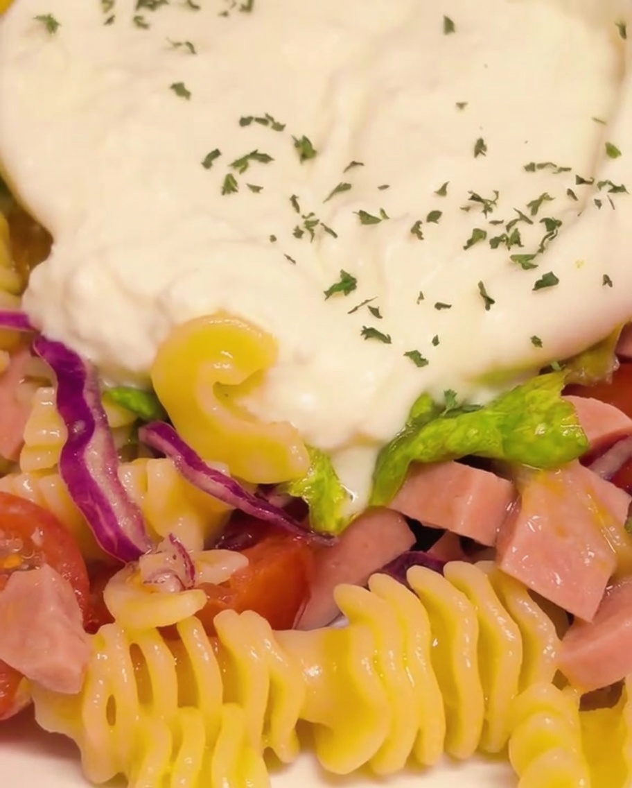 Primer plano del queso burrata cremoso y abierto sazonándose con perejil verde finamente picado y hojuelas de pimiento rojo.