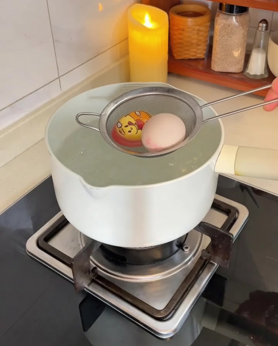 Huevos bajados cuidadosamente a una olla de agua hirviendo con un colador de malla de acero inoxidable.