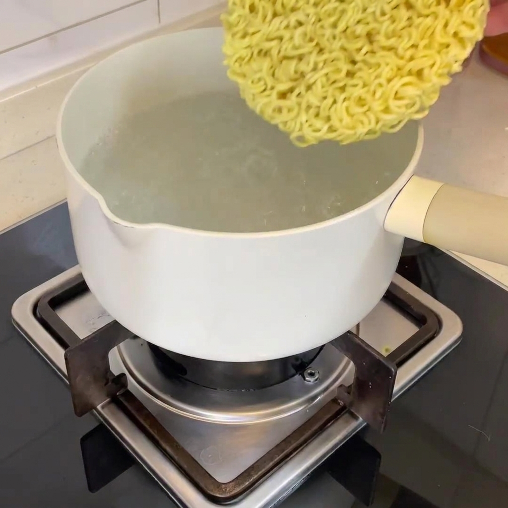 Un bloque de fideos ramen secos cayendo en una olla de agua hirviendo.