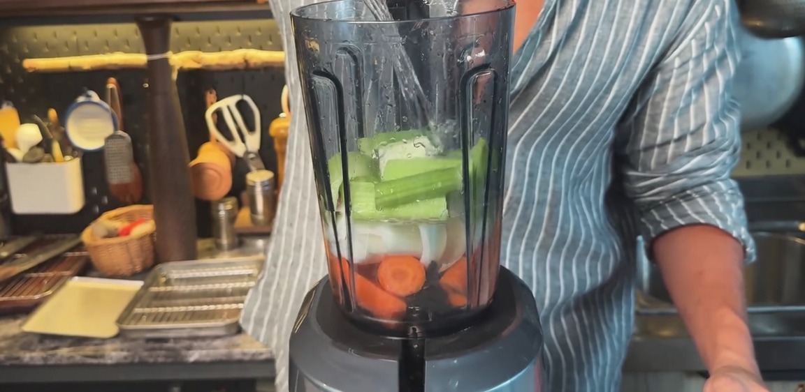 Vertiendo agua en una licuadora con zanahorias, cebollas y apio troceados.
