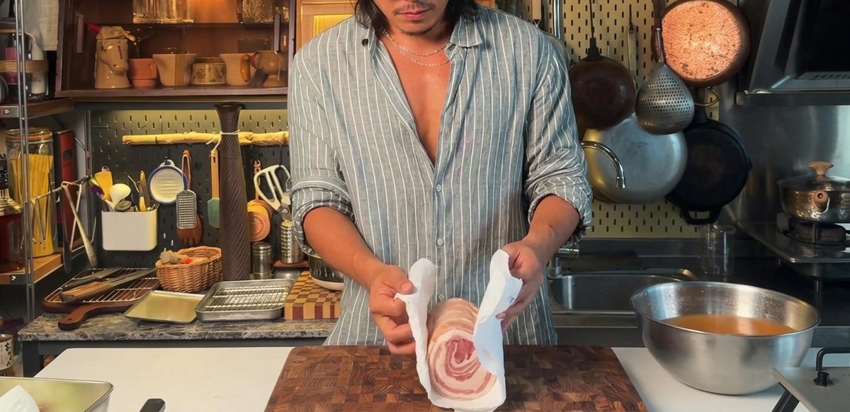 Secando con papel de cocina una panceta de cerdo atada y marinada.