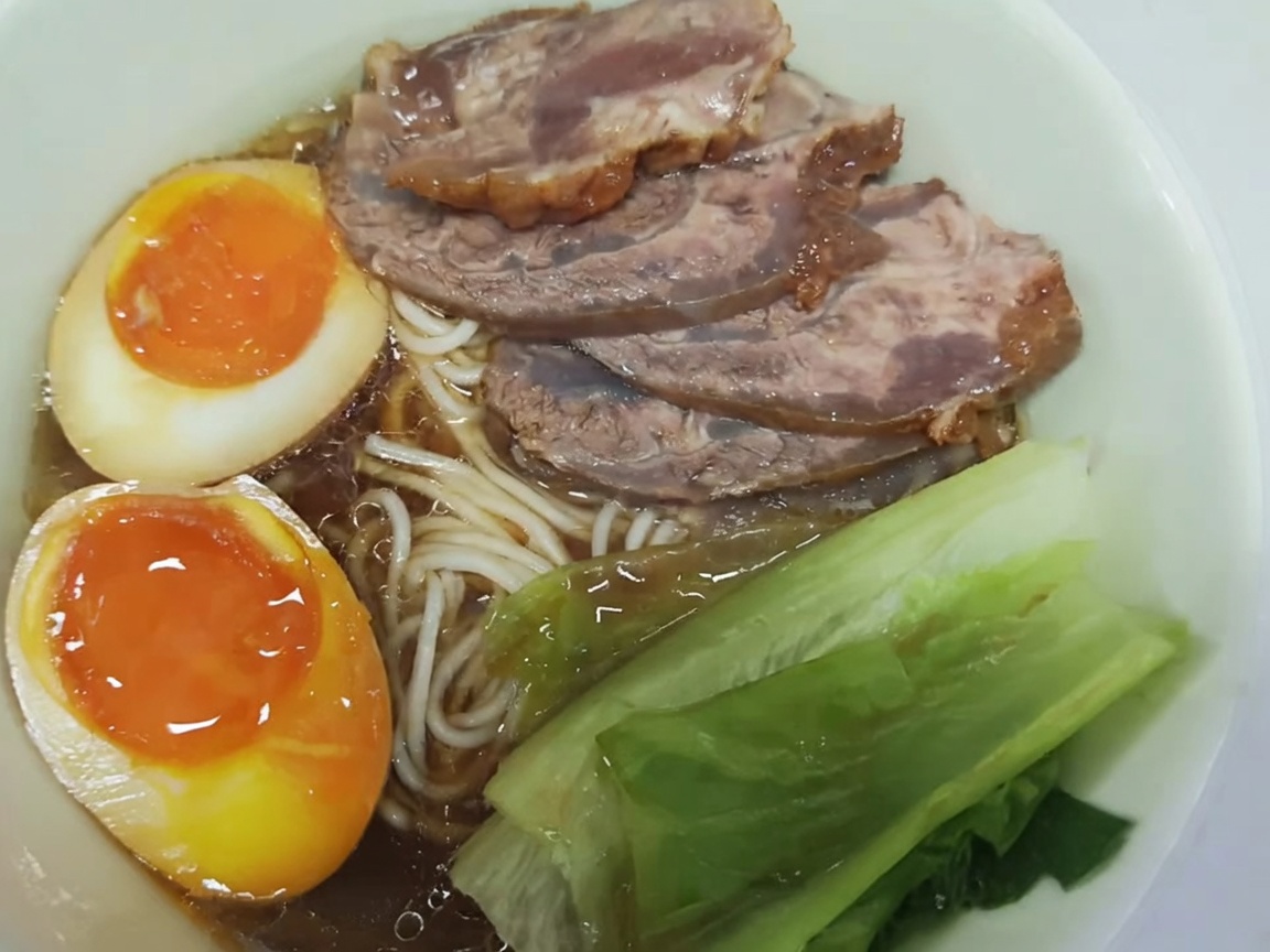 Un morcillo de ternera crudo en una olla de barro rodeado de jengibre fresco y cebolletas.
