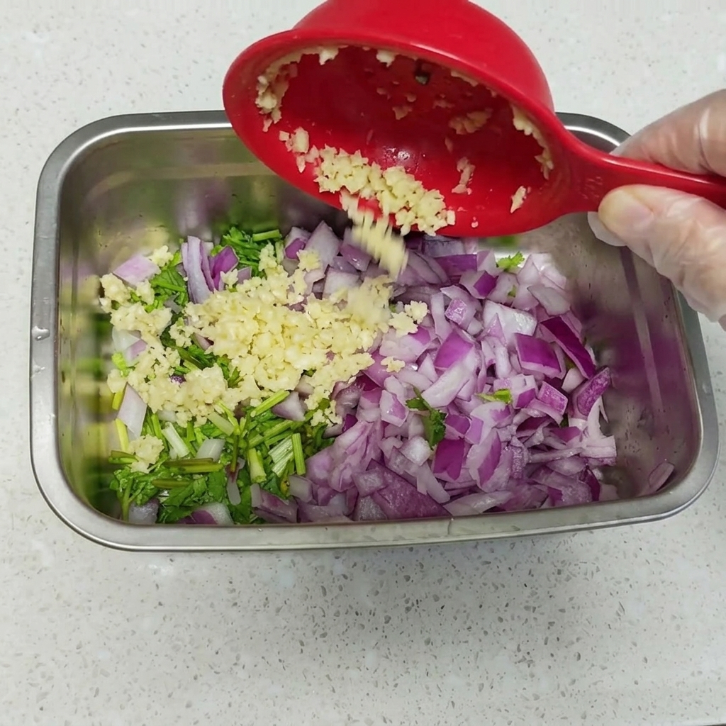 Primer plano de huevos pasados por agua pelados sobre una cama de cilantro, cebolla roja y ajo picado en un recipiente de metal.