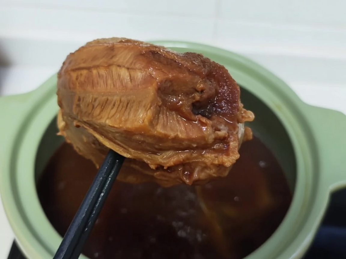 Un morcillo de ternera cocinado siendo envuelto firmemente en film transparente.