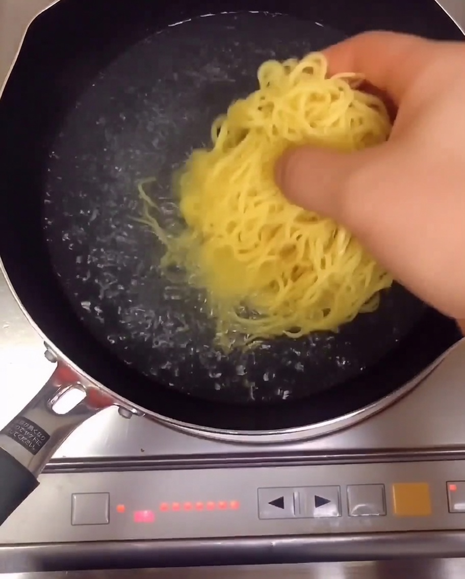 Fideos ramen amarillos hirviendo en una olla con agua.