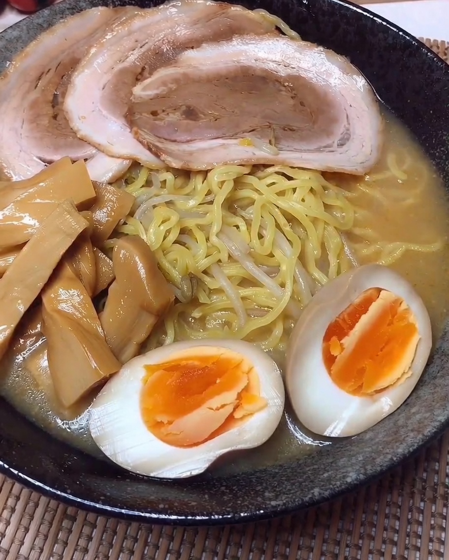 Tazón de ramen con filas ordenadas de cerdo, brotes de bambú y huevo.