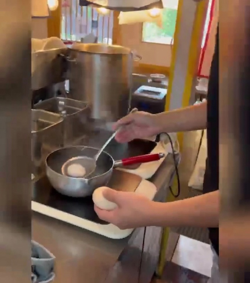 Persona usando un colador para introducir suavemente huevos blancos en una olla con agua hirviendo.
