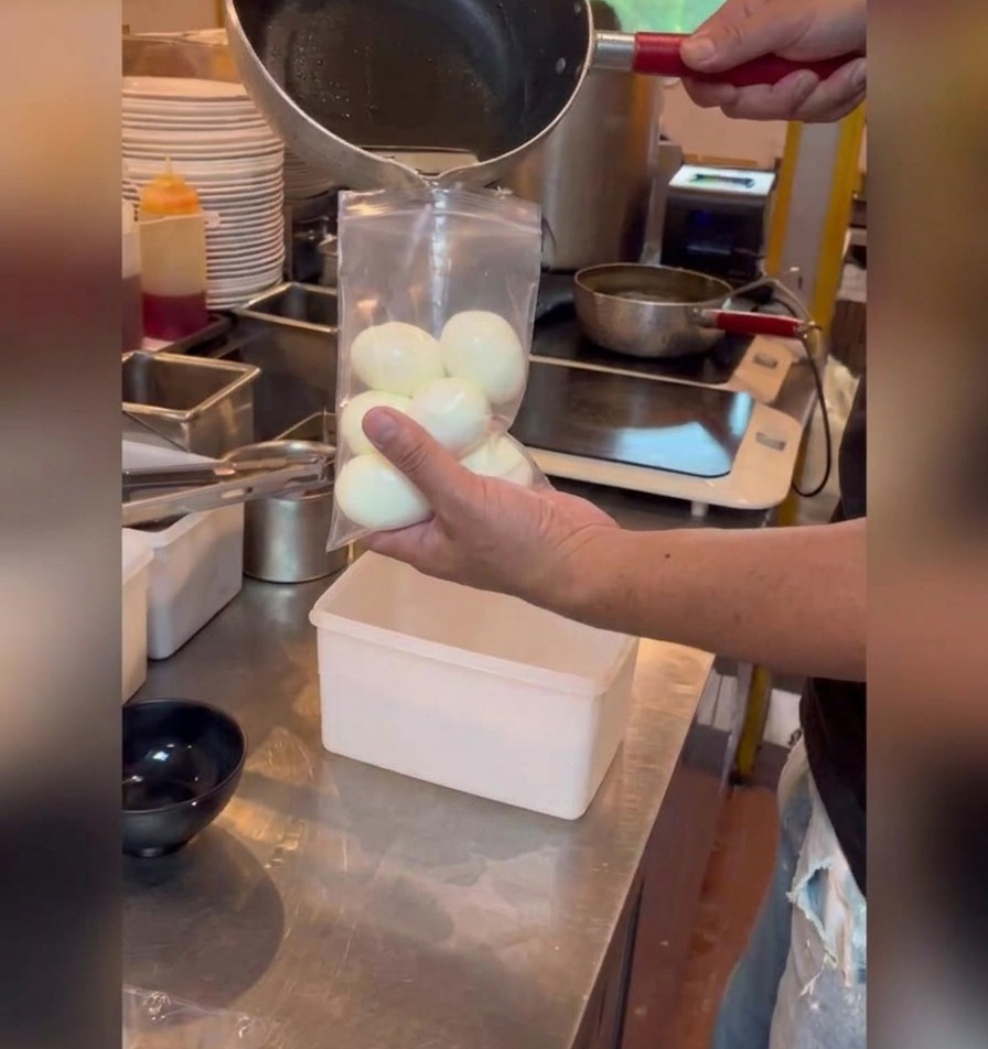 Vertiendo una marinada oscura a base de soja desde una pequeña cacerola a una bolsa de plástico con huevos pelados.
