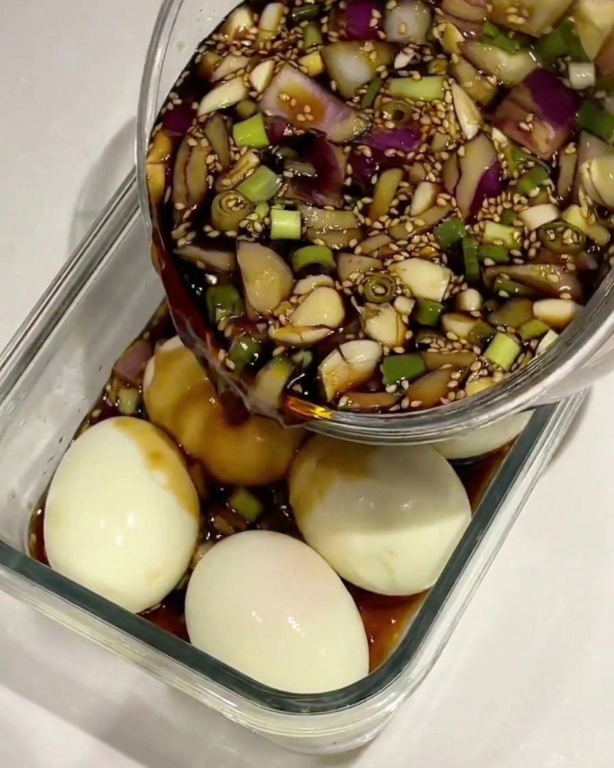 Marinado de salsa de soja siendo vertido sobre huevos cocidos y pelados en un recipiente de cristal.