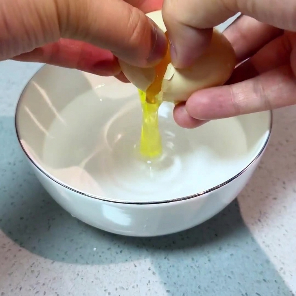 Dos manos rompiendo cuidadosamente un huevo fresco en un cuenco pequeño con agua clara.