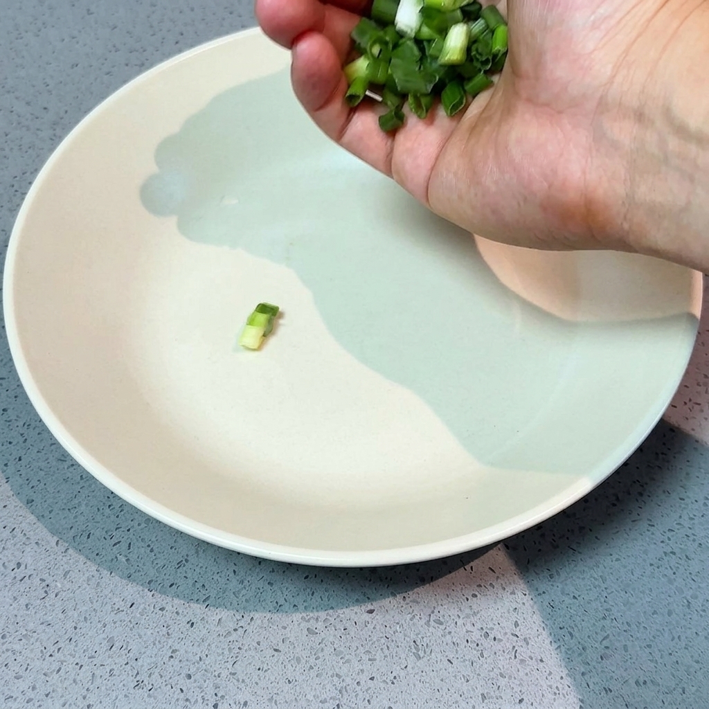 Una mano esparciendo cebollino fresco picado en un cuenco grande y blanco.