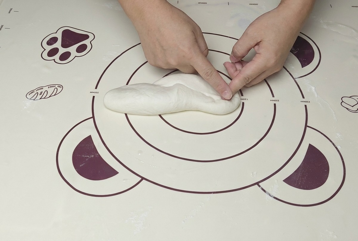 Manos amasando una bola de masa usando el talón de la mano para presionar con firmeza.