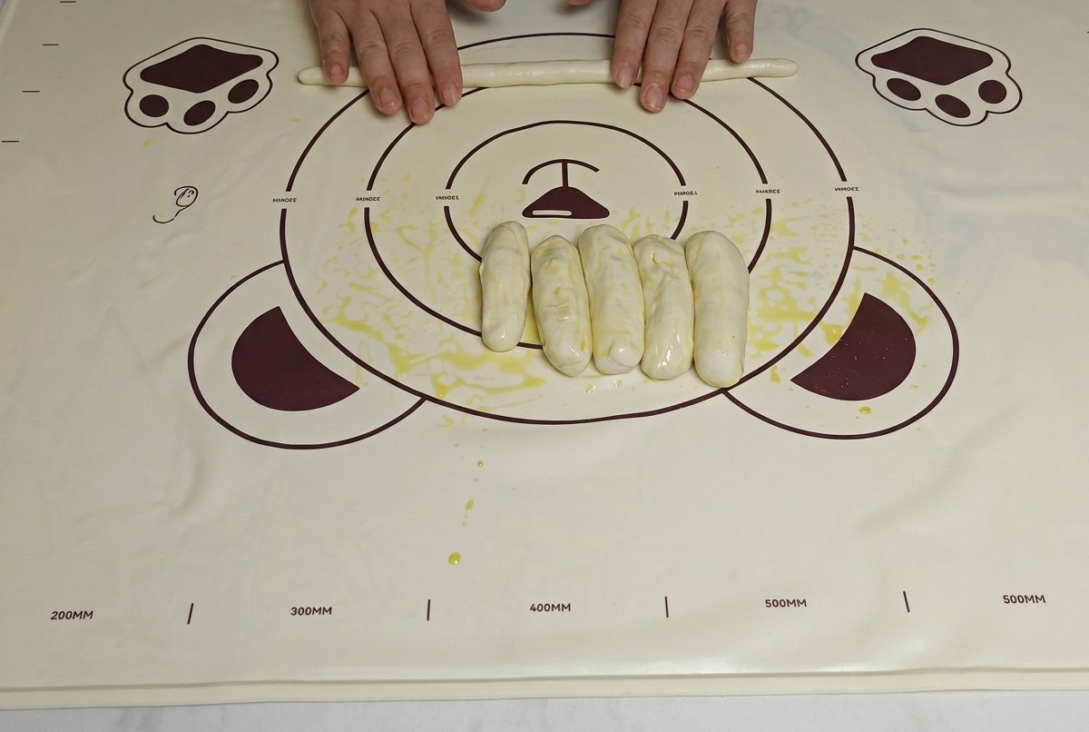 Manos estirando tiras de masa aceitada sobre un tapete, haciéndolas más largas y delgadas.