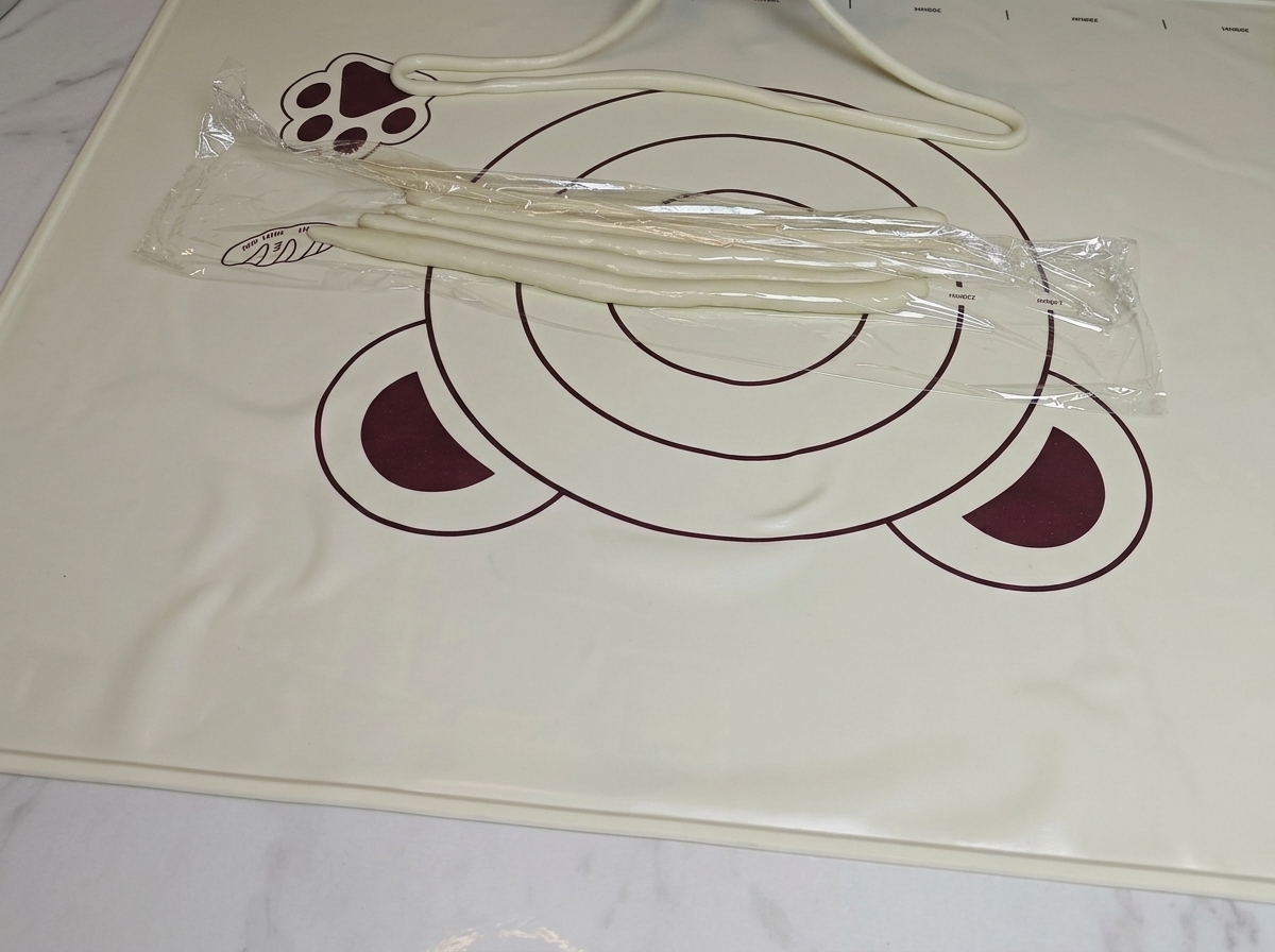 Manos estirando cuidadosamente una tira de masa preparada para convertirla en un fideo largo.